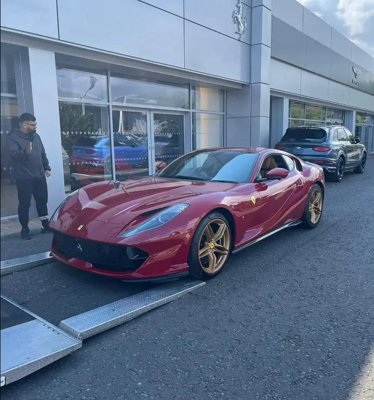 Red Ferrari beside vehicle loading ramps outside a dealership