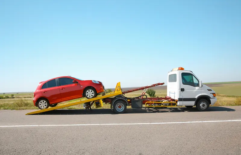 Red hatchback being loaded onto a flatbed recovery truck