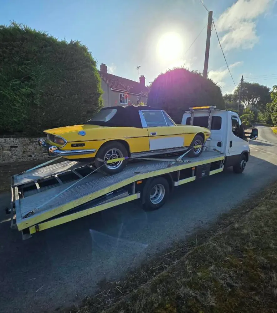 Yellow classic convertible secured on a flatbed car transporter on a country road