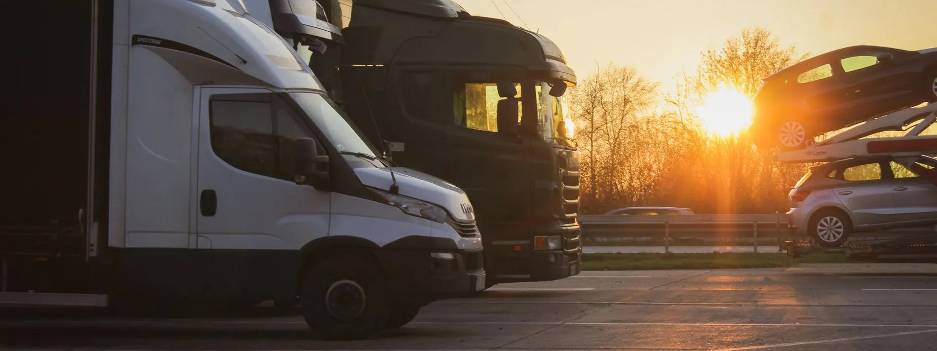 Vehicle transporters and delivery trucks parked at sunset