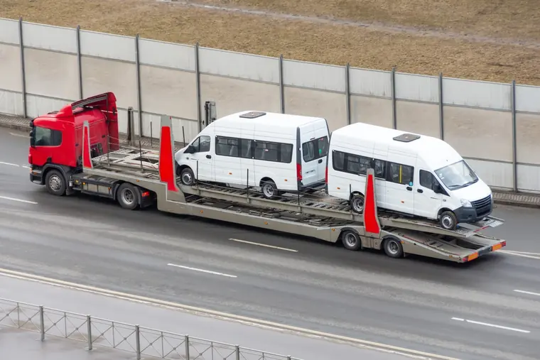 Two white vans secured on a multi-vehicle transporter