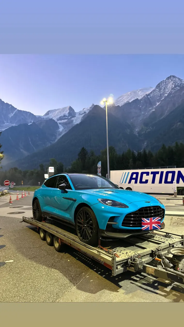 Aston Martin on a transport trailer beneath mountain scenery